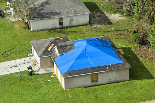 Top view of leaking house roof covered with protective tarp sheets against rain water leaks until replacement of asphalt shingles.